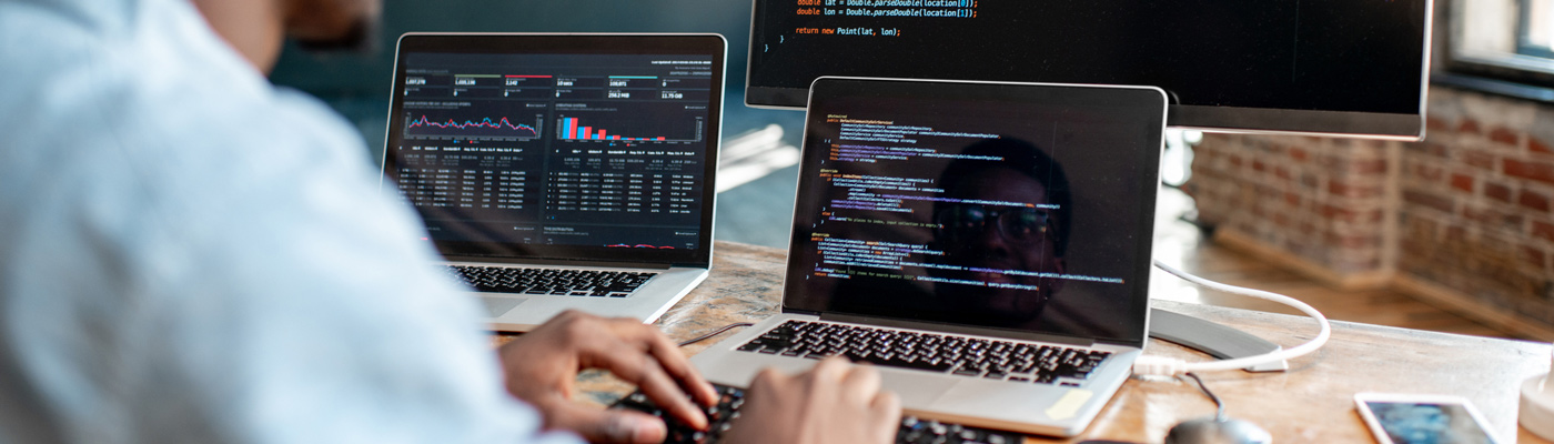 Programmer editing code on three Macs