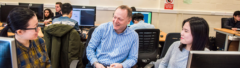 Professor talking to two students around computer screens